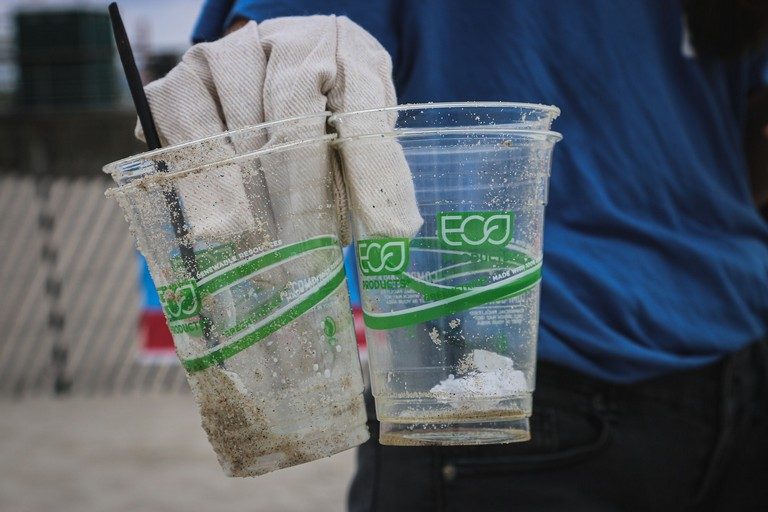 An image of a person holding plastic cups in their hand. Plastic cups have "eco" written on them.